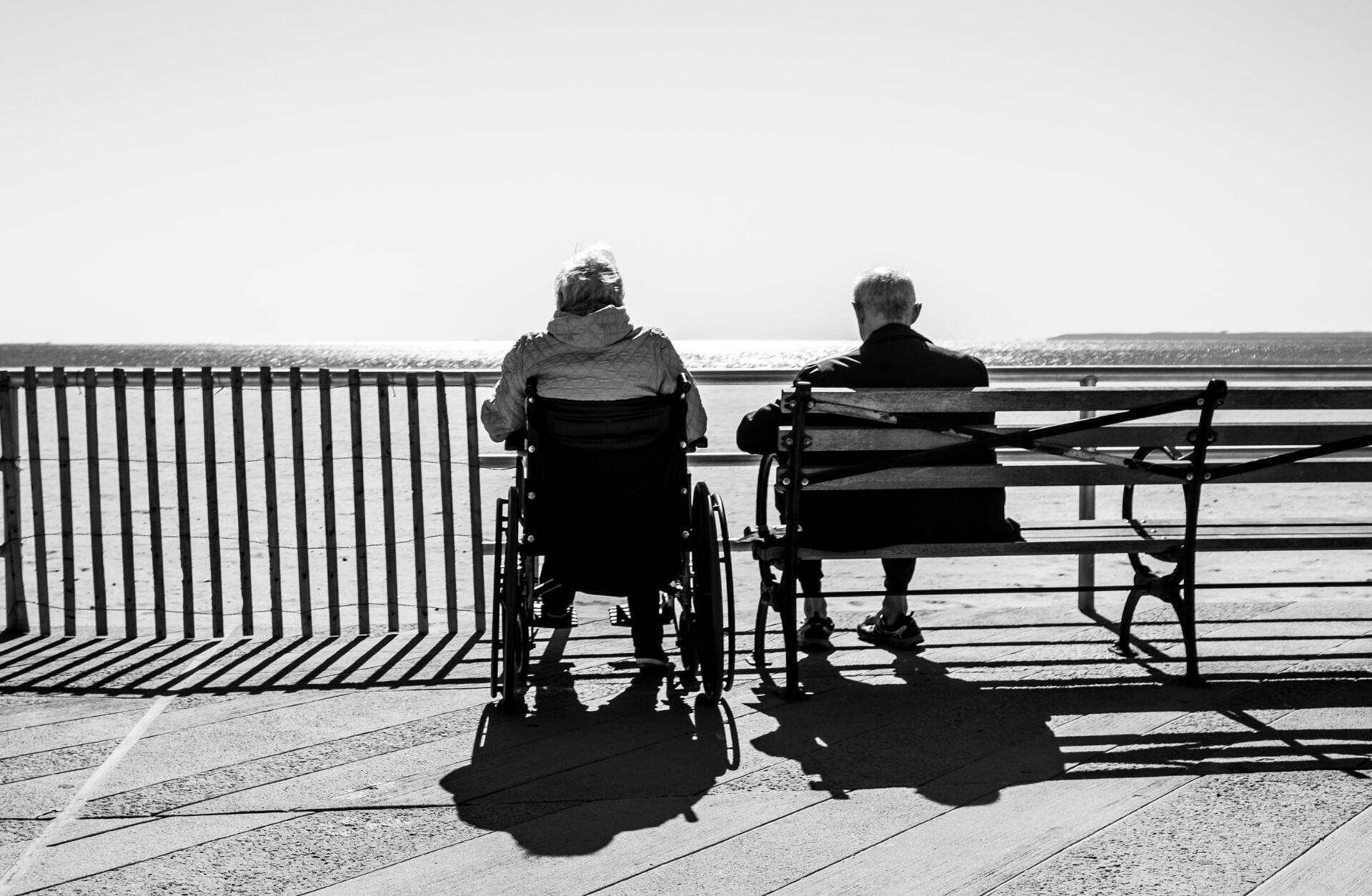 Elderly couple sitting, one on a wheelchair.