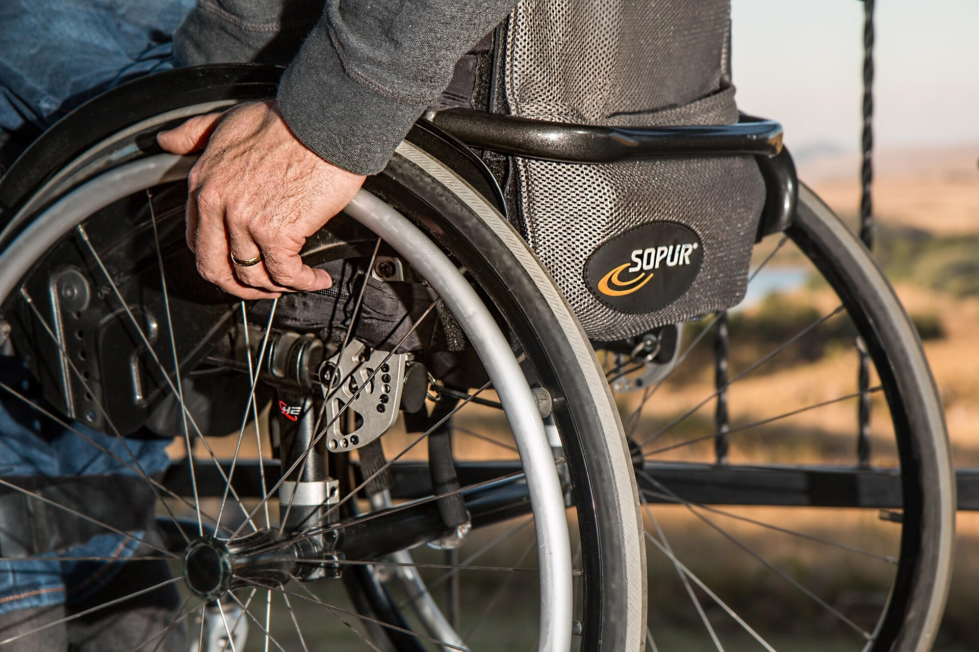 Back of wheelchair with an elderly male hand with wedding ring grabbing on to the wheel